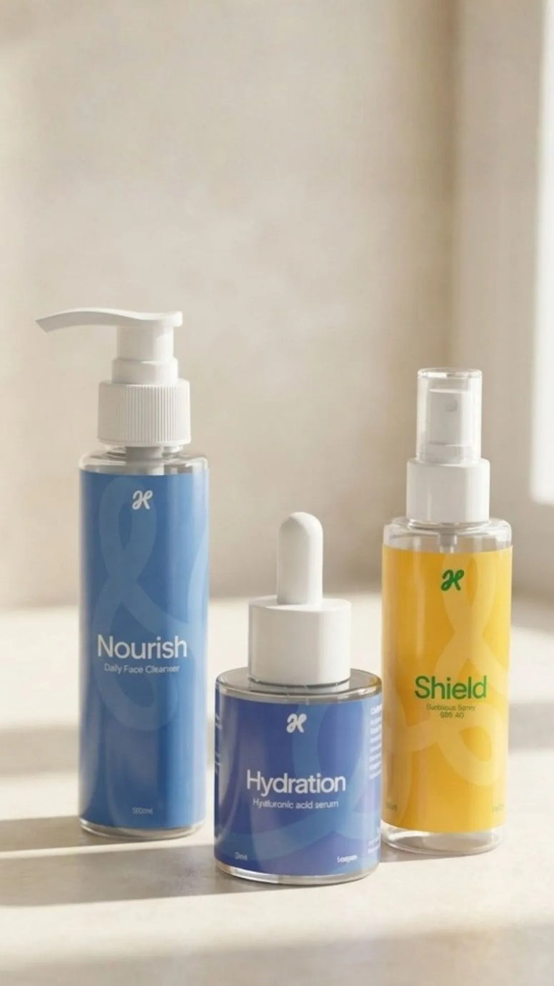 Three skincare products from the brand 3A are arranged on a white surface against a warm beige background with soft sunlight and shadows. The products are: a white tube labeled 'Nourish' with pink text, a blue dropper bottle labeled 'Hydration' with white text, and a yellow spray bottle labeled 'Shield' with green text.